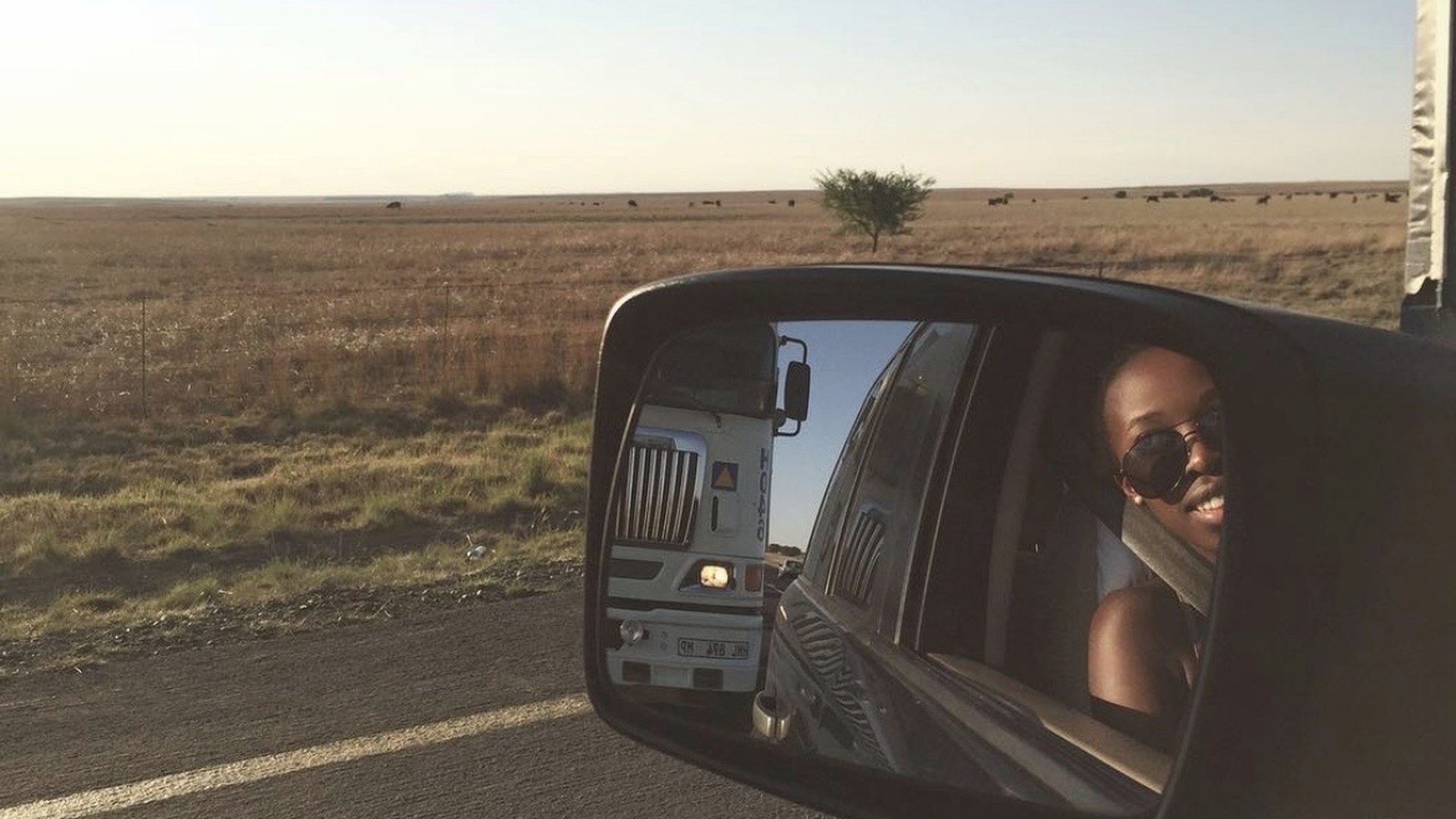 A traveller smiling in a car mirror on an open road